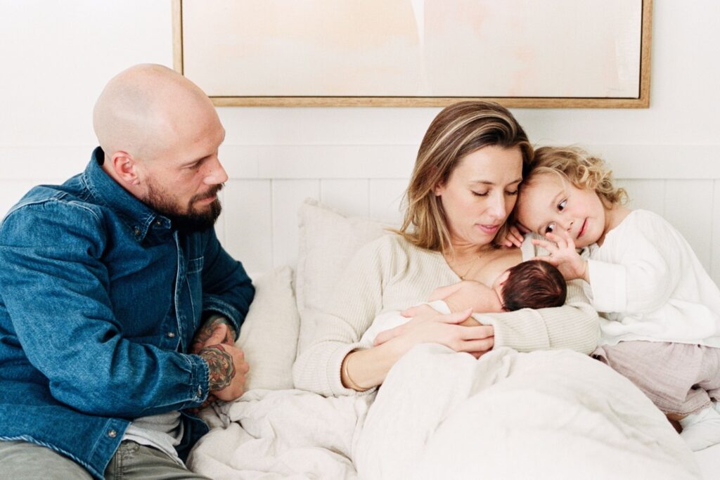 Family cuddle on the bed with newborn and older sibling during a relaxed in-home newborn session in Sydney