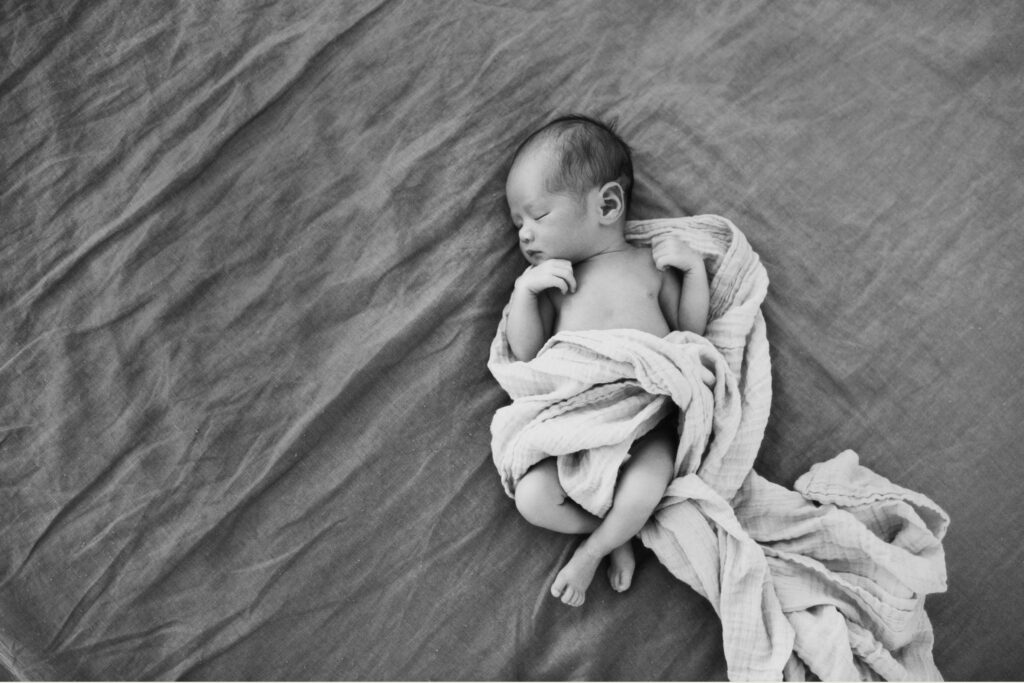Black and white in-home newborn photo in Sydney of a sleepy newborn swaddled on the bed