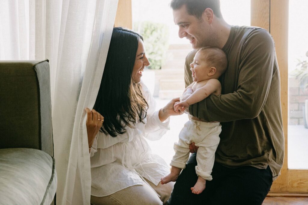 Lifestyle baby photos in Sydney of parents interacting with their baby near a window at home