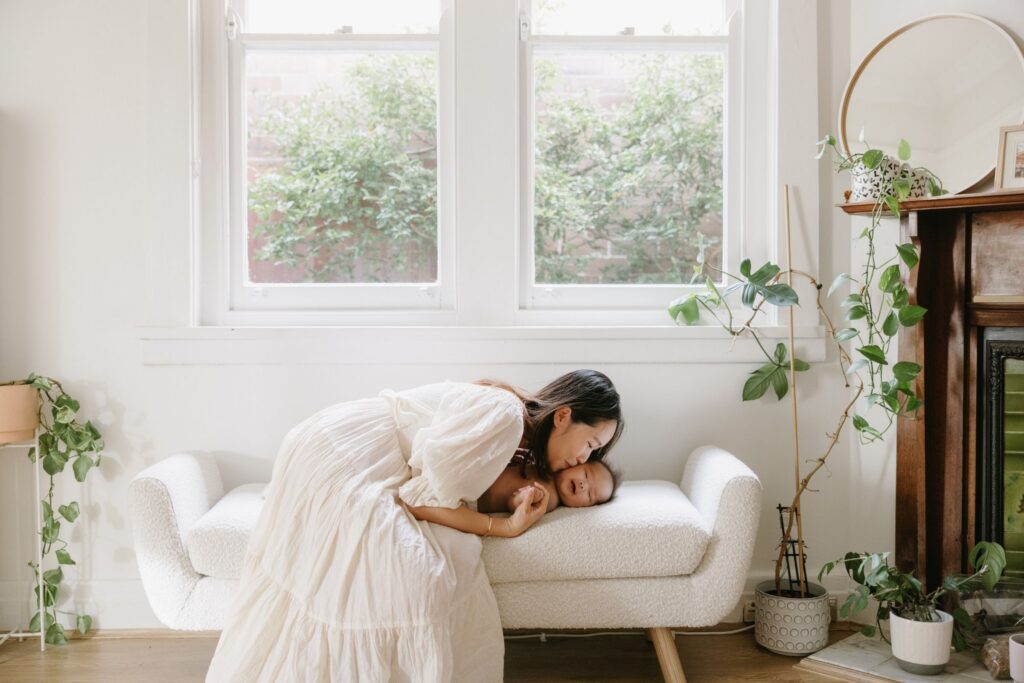 Mum resting with her newborn on a lounge by soft window light during an in-home newborn photography session in Sydney.