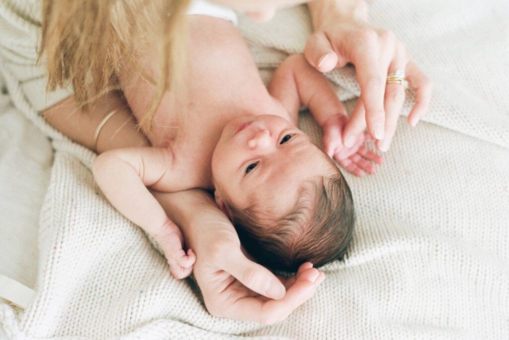 Close-up newborn baby photo in Sydney of baby lying on a soft knit blanket with parent’s hands nearby