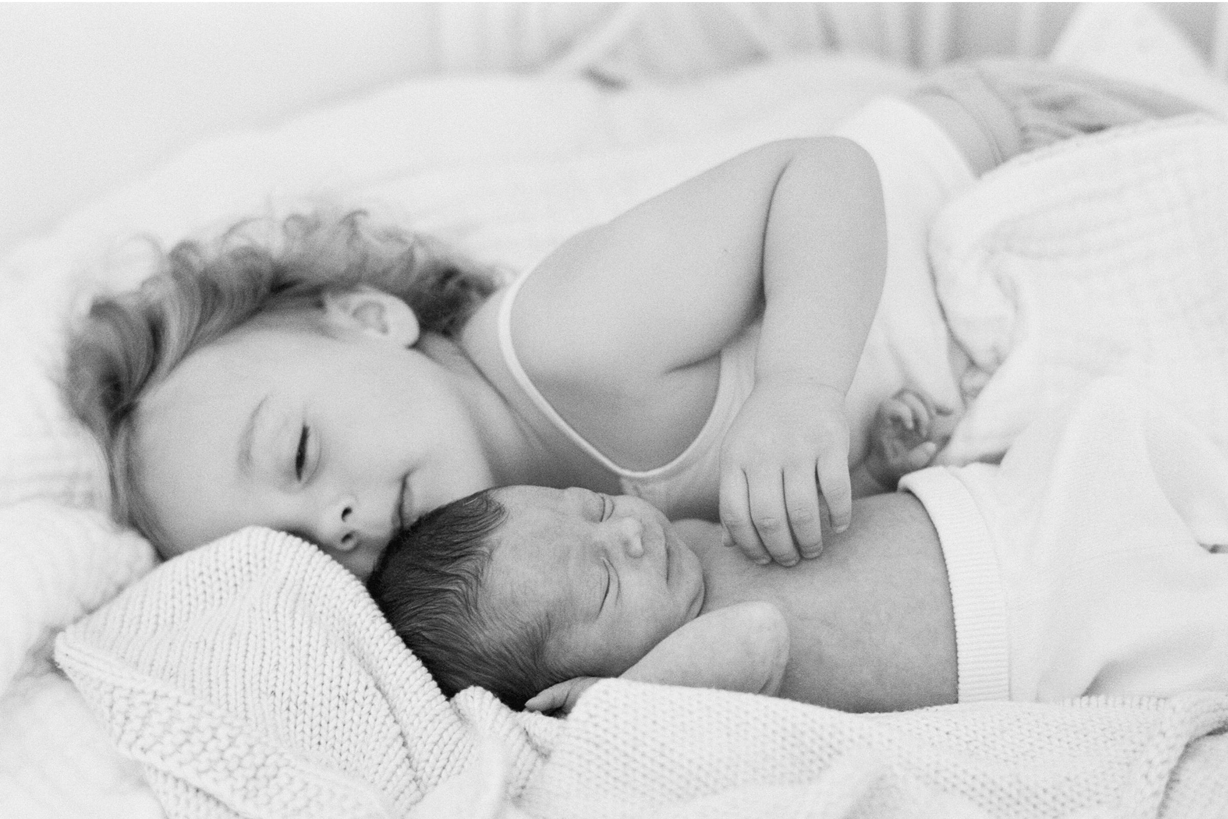 Older sibling cuddling newborn on the bed during a cosy in-home newborn session in Sydney.