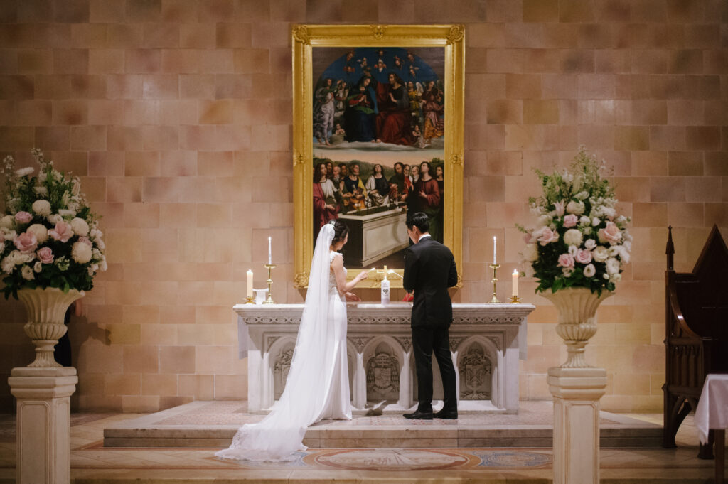 Couple exchanging vows at a church altar decorated with white florals, captured in warm documentary style by Sydney wedding photographer Tealily Photography