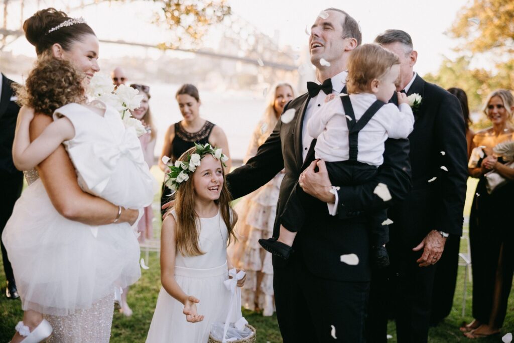 Joyful wedding exit with flower girl tossing petals as couple laughs in golden light — documentary wedding photography Sydney by Tealily Photography

