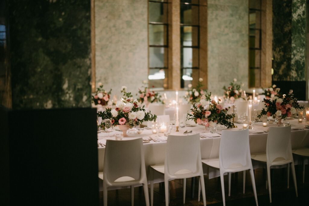 Elegantly styled long reception table with white chairs, pink floral centrepieces, and soft natural light through stone archway windows — intimate Sydney wedding venue photographed by Tealily Photography