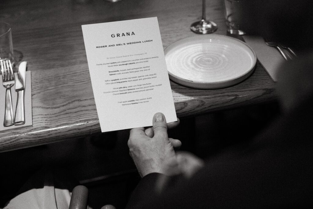 Black and white close-up of a guest holding a Grana menu card over a place setting — intimate restaurant wedding detail photographed by Tealily Photography Sydney