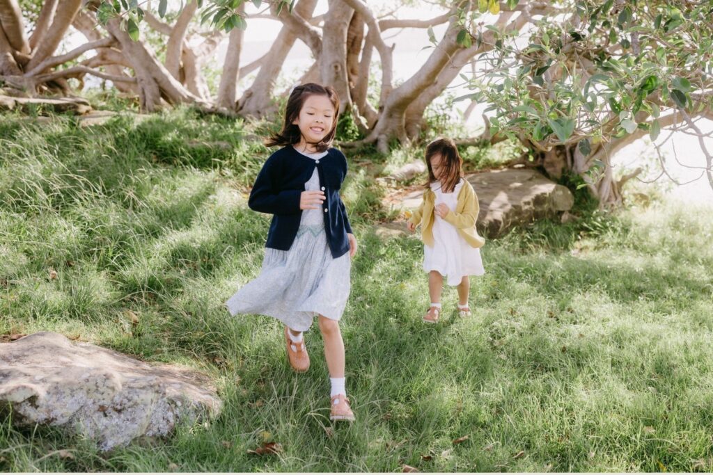 Two sisters running through long grass at balmoral beach