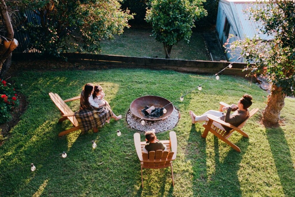 A family on holiday in Sydney in winter sitting around a firepit as the sun sets