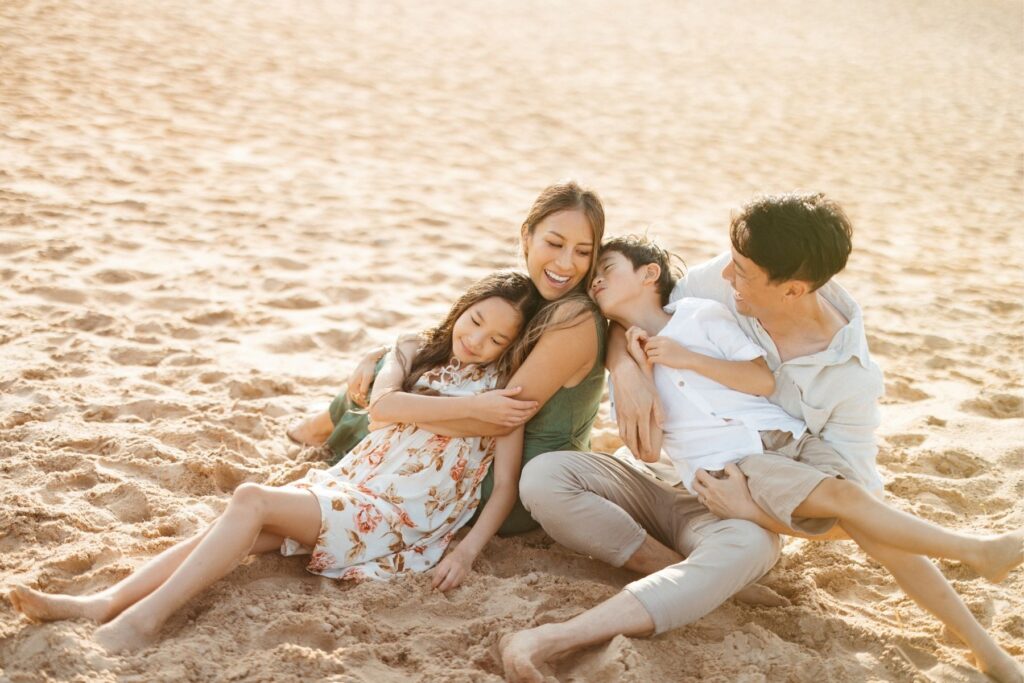 A relaxed family of four on holiday in Sydney joyfully entangled on the beach bathed in golden light