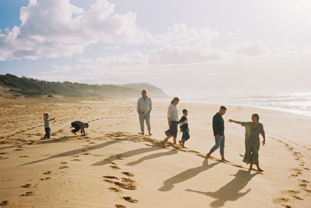 A three generational family sessions captured at the beach with the mother at the front reaching out her hand to her youngest son at the back of the frame