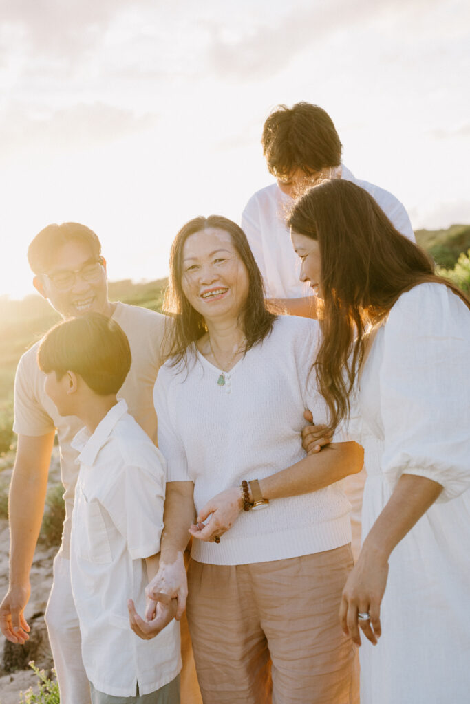 A grandma with her daughter and grandchildren smiling at the camera with golden light framing her face