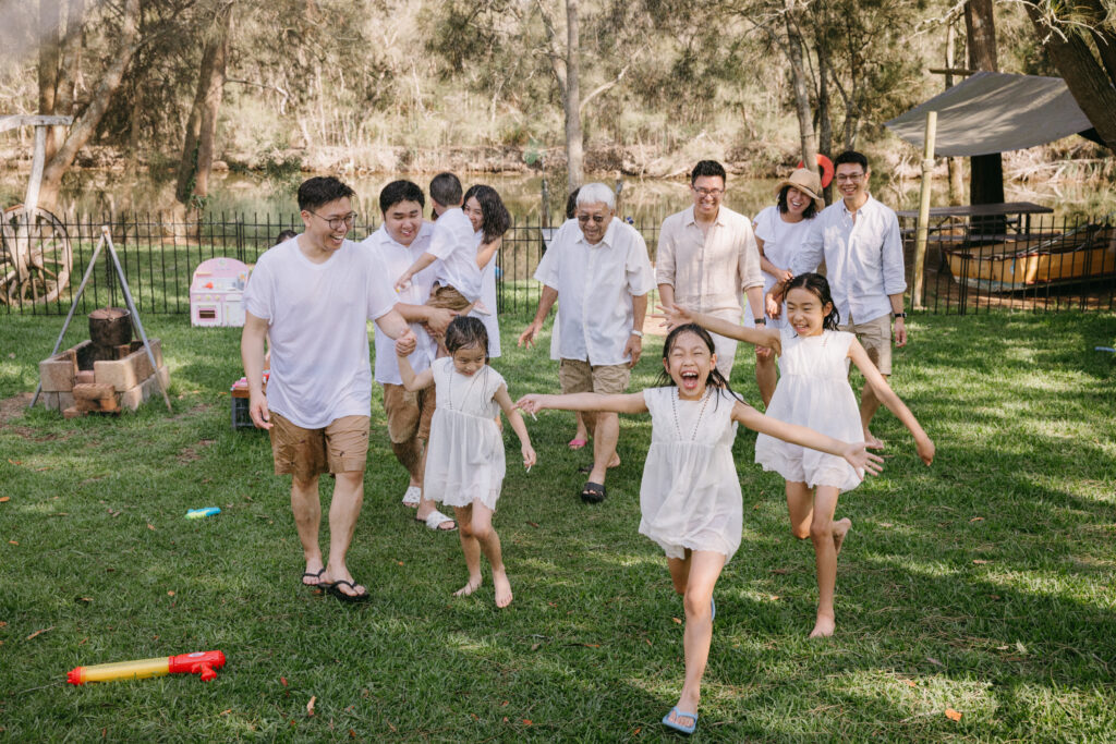 Three generations of family gathered together and running through the sprinkler on a hot summer day