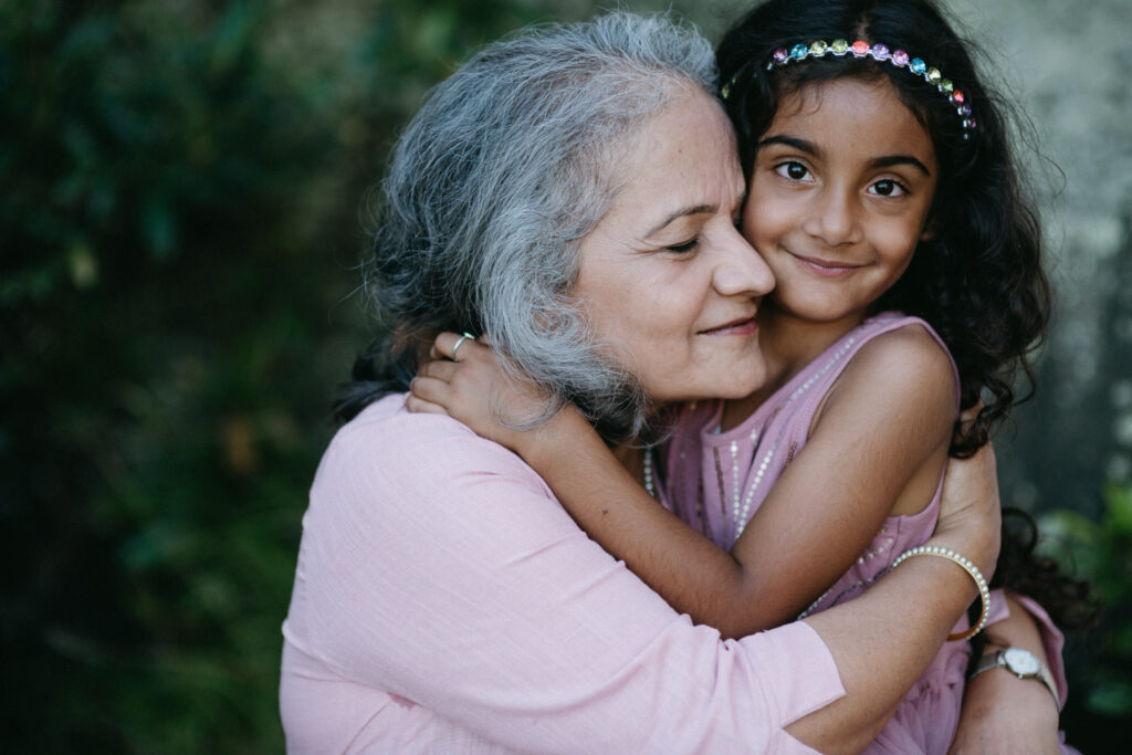 A little girl with her arms wrapped around her grandma and looking directly at the camera