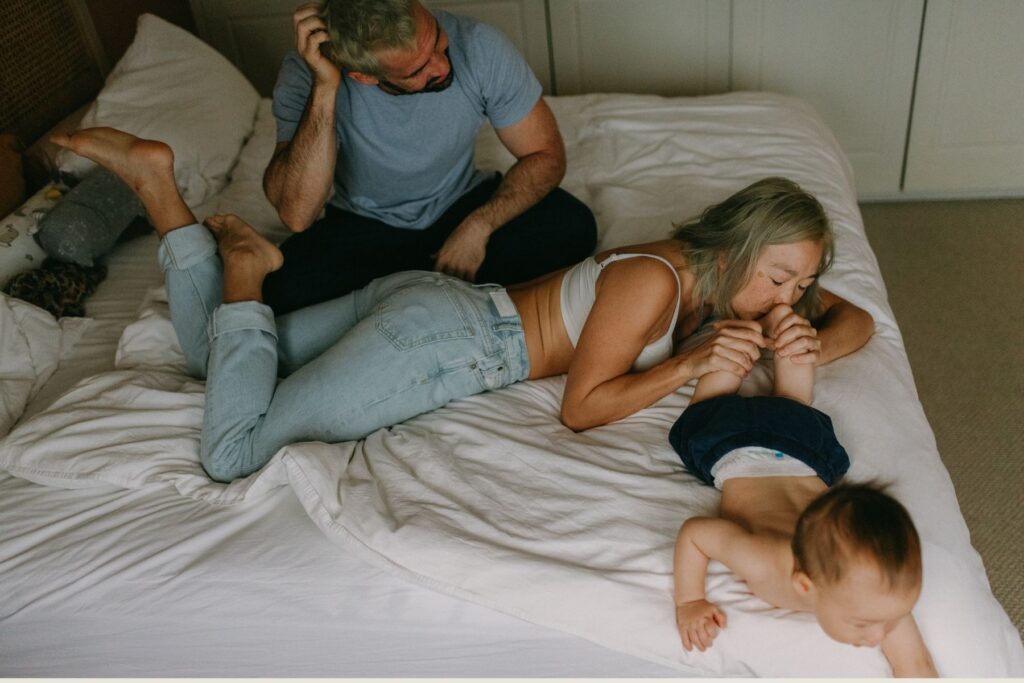 A family relaxing on the bed chasing their young toddler during an at home documentary photoshoot